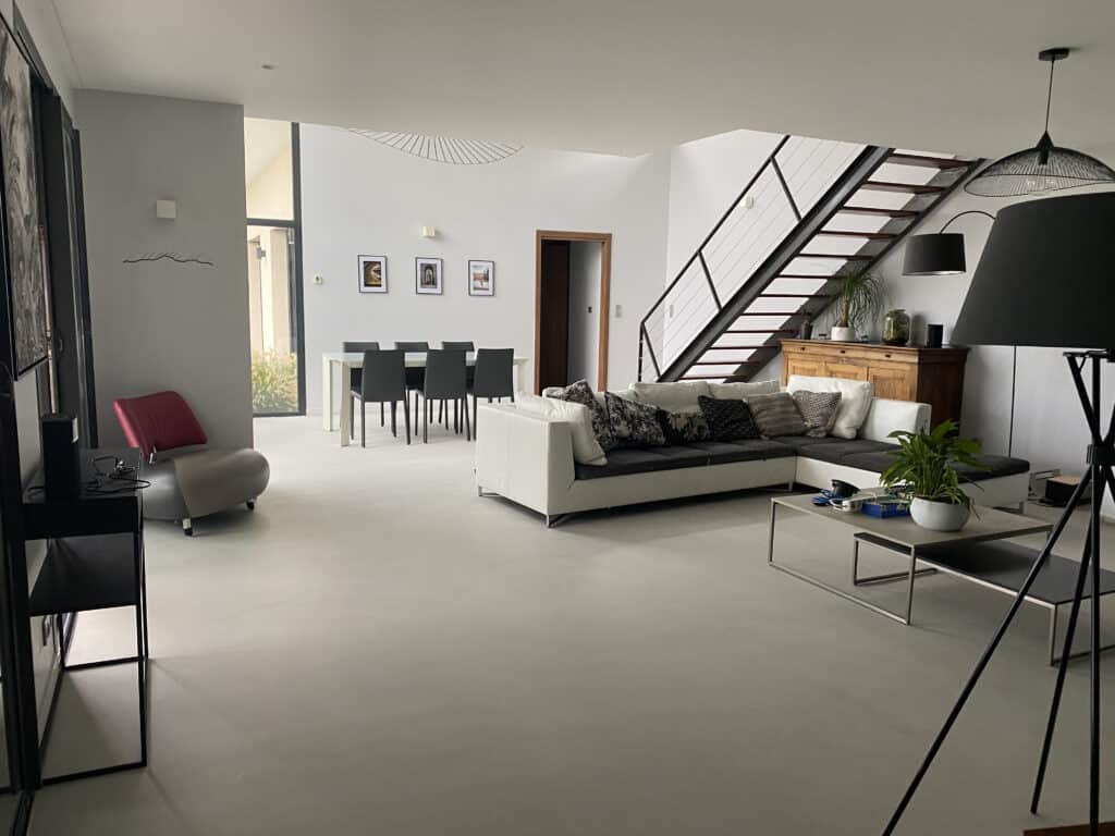 Salon et salle à manger modernes, ambiance ouverte et lumineuse. Canapé blanc, table noire, escalier contemporain et mobilier épuré.