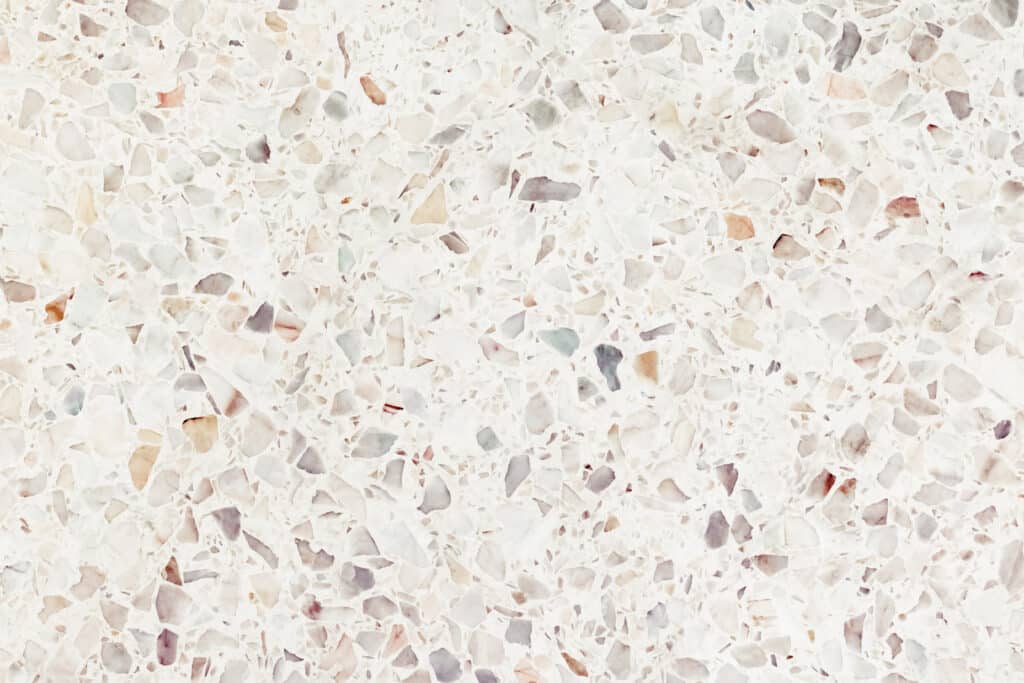 Texture de terrazzo blanc avec des éclats de marbre multicolores : gris, beige, rose pâle et bleu-vert, formant une surface mouchetée.