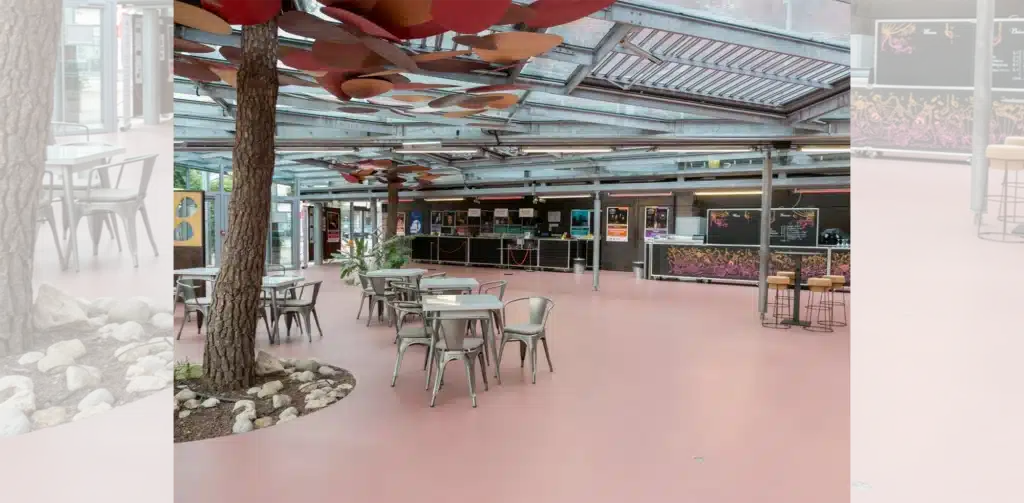 Hall d'accueil avec sol rose, tables en métal, arbres intérieurs et comptoirs d'accueil mentionnant 'ACHAT'.