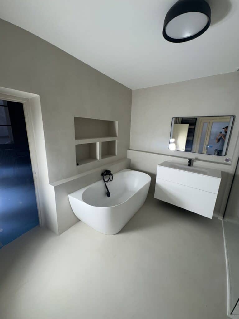Salle de bain moderne avec baignoire îlot, vasque suspendue blanche et niches de rangement murales.