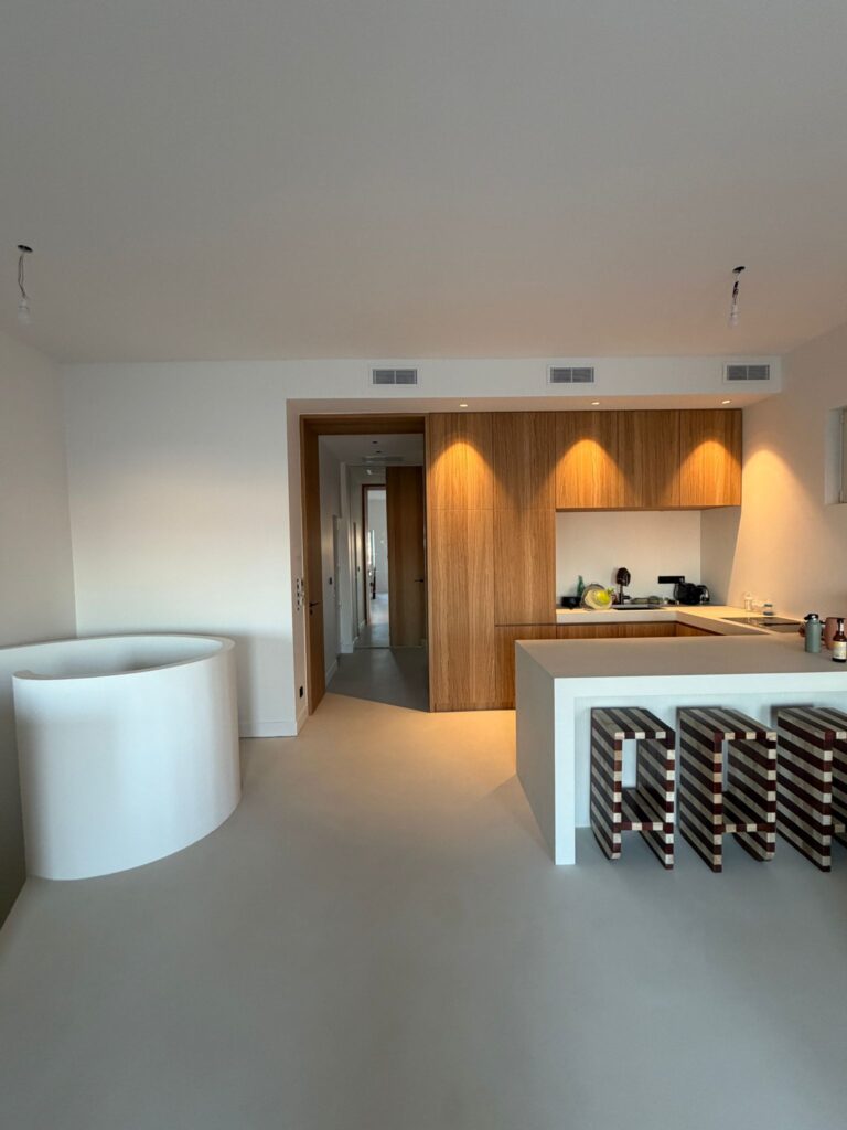 Cuisine moderne minimaliste avec meubles en bois, îlot blanc et tabourets design dans un intérieur épuré et lumineux.