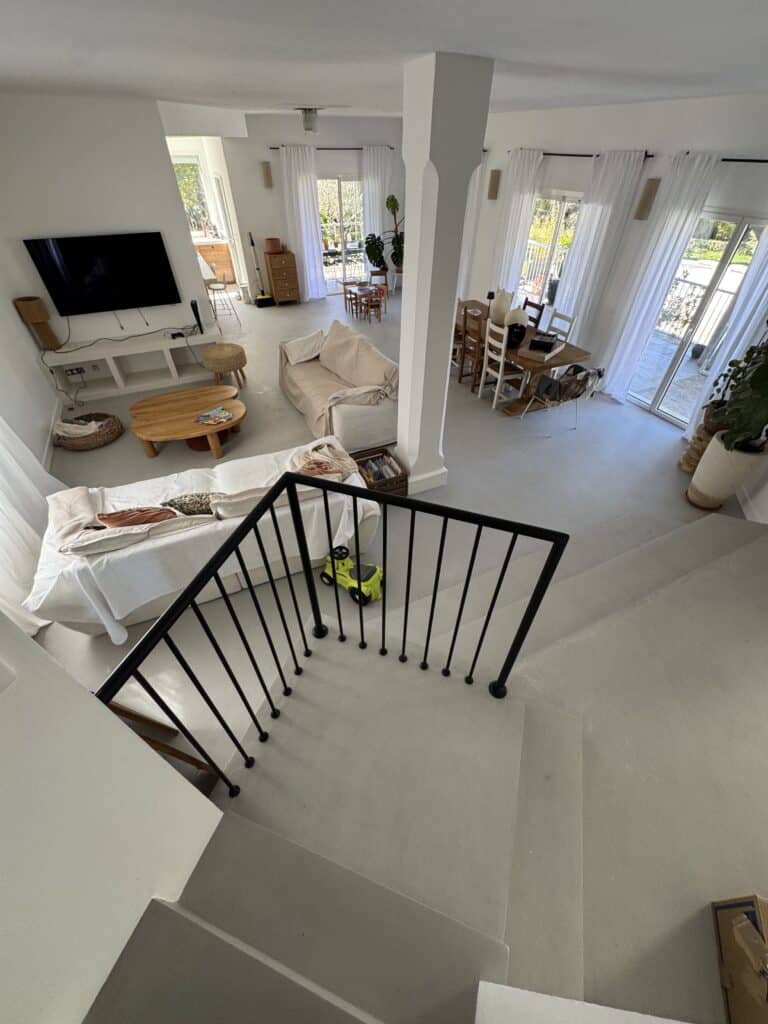Vue plongeante sur un salon bohème chic avec canapés, table en bois et escalier à rampe noire.