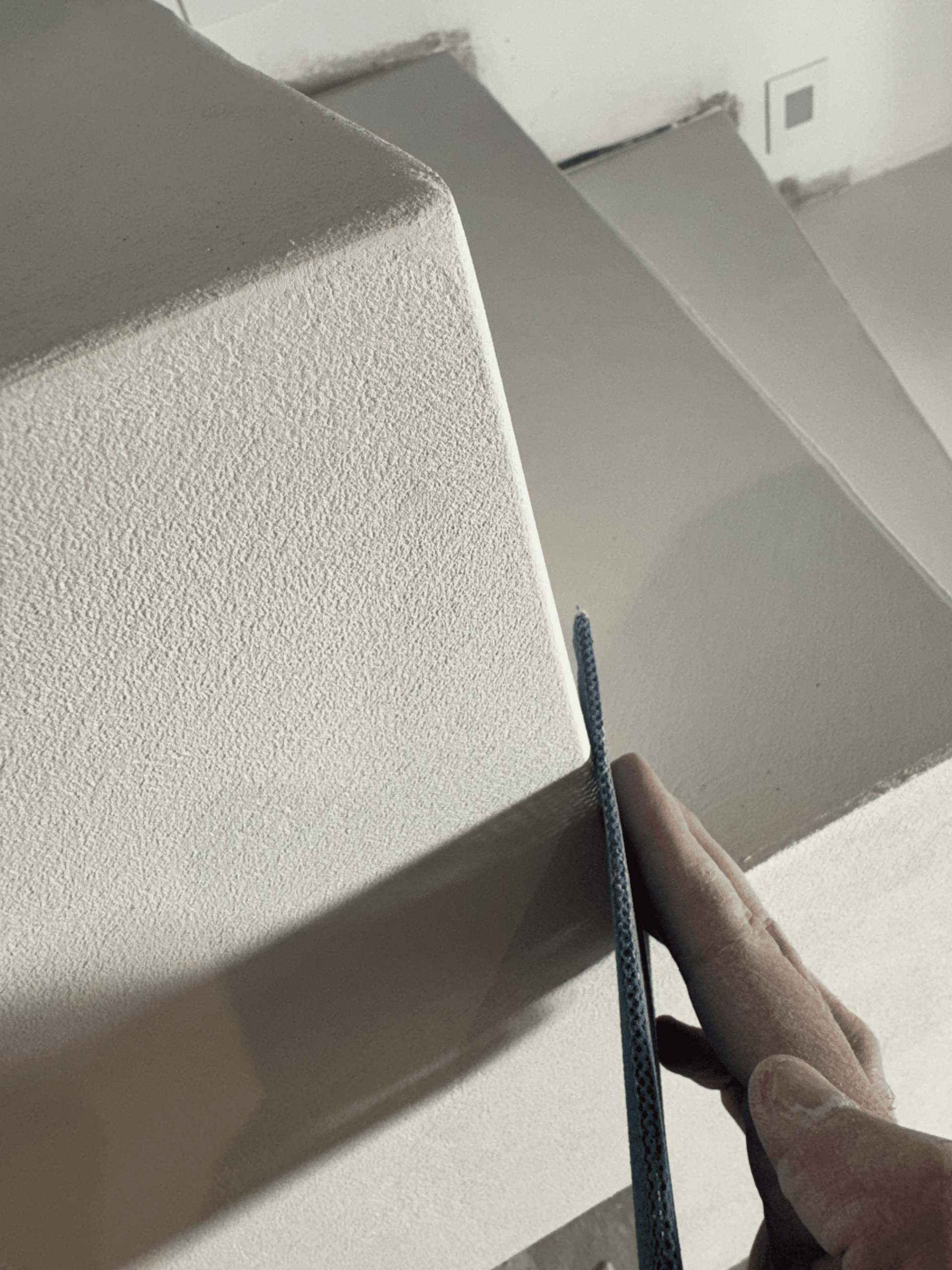 Ponçage de finition sur enduit texturé blanc intérieur Main ponçant l'angle d'un mur à l'enduit texturé blanc pour des finitions de rénovation soignées.