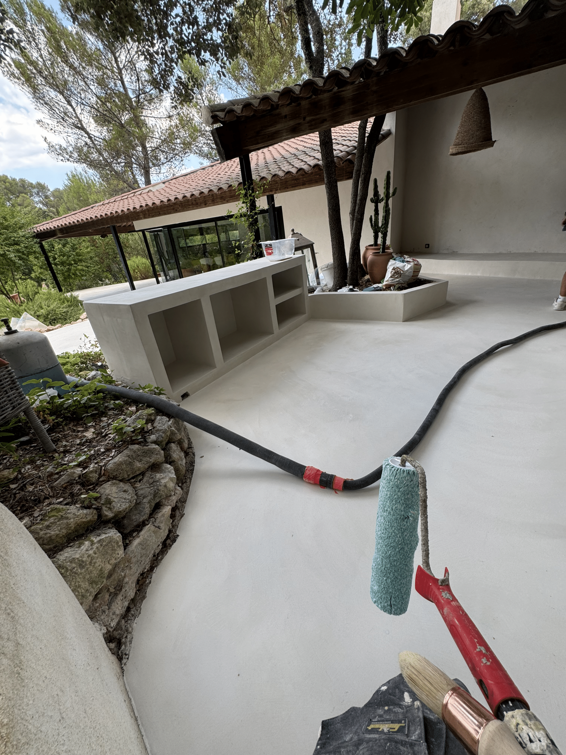 Rénovation de Terrasse en Micro-ciment Moderne et Design Application de micro-ciment sur une terrasse extérieure avec comptoir de cuisine moderne et rouleau de peinture.